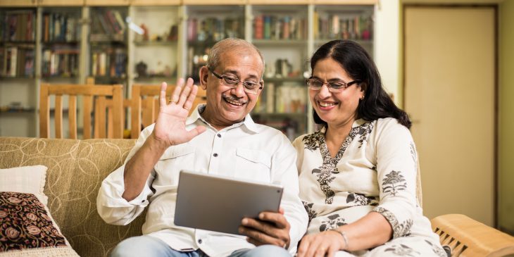 Senior couple video chatting on tablet while sitting on a couch at home