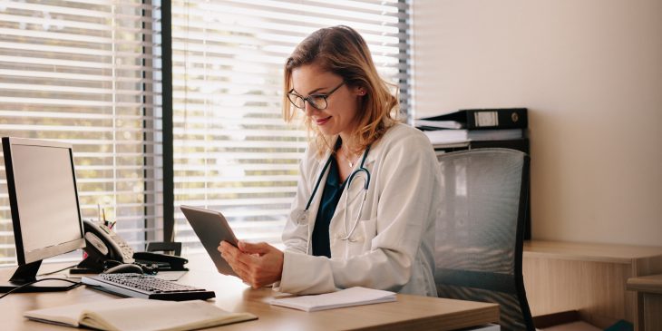 Female doctor using a digital tablet at her desk in the clinic. Female doctor working on her tablet pc in her office.