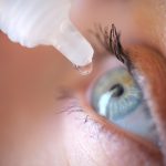 Drops from vial dripping into woman eye closeup