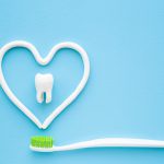 Toothbrush with green bristles on pastel blue background. Heart shape created from paste. White tooth in middle of heart. Love healthy teeth. Empty place for text, quote, sayings or logo. Closeup.