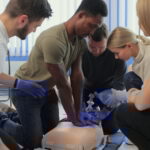 Closeup of students practicing CPR chest compression on dummy.