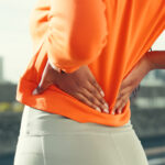 Medical Moment: Don’t Wait to Address Back Pain Fitness, hands and woman in city with back pain, muscle fatigue and sprain from overexertion. Runner, stretching and outdoor with physical ache, sciatica symptoms or repetitive stress injury in spine
