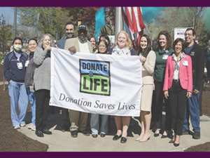 Group of people standing outdoors holding a Donate Life banner that reads “Donation Saves Lives.”